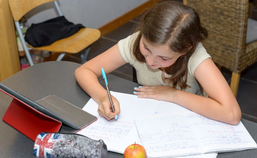 A young girl at Henrietta Barnett School diligently writes on a notebook, focusing on her task