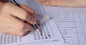 A person writing on a test paper with a pencil, highlighting differences between CEM and GL