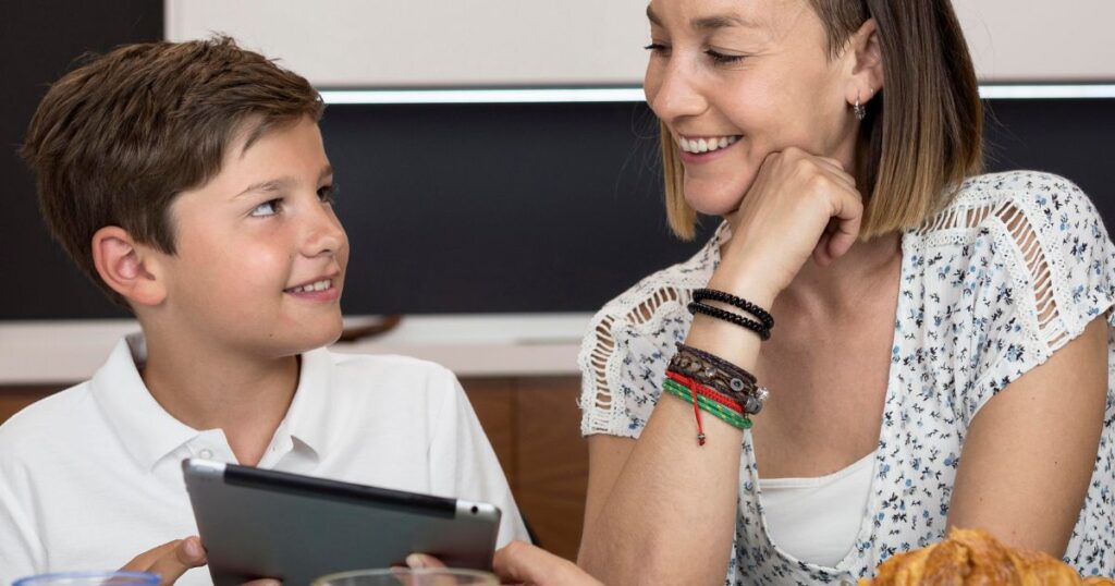 A woman and boy sitting at a table with a tablet, participating in the 'Verbal Virtuosity: Language Proficiency in Tiffin Mock Test